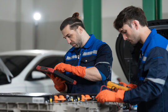 Electric vehicle car services. EV car. Diagnostic battery pack. Team of technician or Mechanic wearing protective gloves diagnosing electric car vehicles battery, component checks at auto workshop