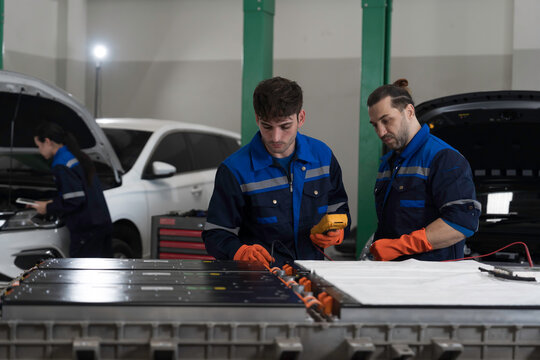 Electric vehicle car services. EV car. Diagnostic battery pack. Team of technician or Mechanic wearing protective gloves diagnosing electric car vehicles battery, component checks at auto workshop
