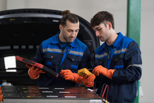 Electric vehicle car services. EV car. Diagnostic battery pack. Team of technician or Mechanic wearing protective gloves diagnosing electric car vehicles battery, component checks at auto workshop
