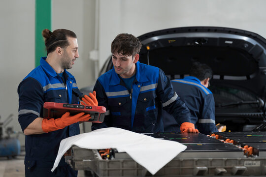 Electric vehicle car services. EV car. Diagnostic battery pack. Team of technician or Mechanic wearing protective gloves diagnosing electric car vehicles battery, component checks at auto workshop