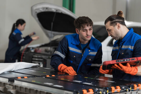 Electric vehicle car services. EV car. Diagnostic battery pack. Team of technician or Mechanic wearing protective gloves diagnosing electric car vehicles battery, component checks at auto workshop