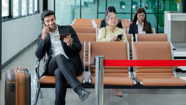 A professional traveler uses a smartphone while waiting with travel documents at a modern airport terminal highlighting mobile communication and business mobility.