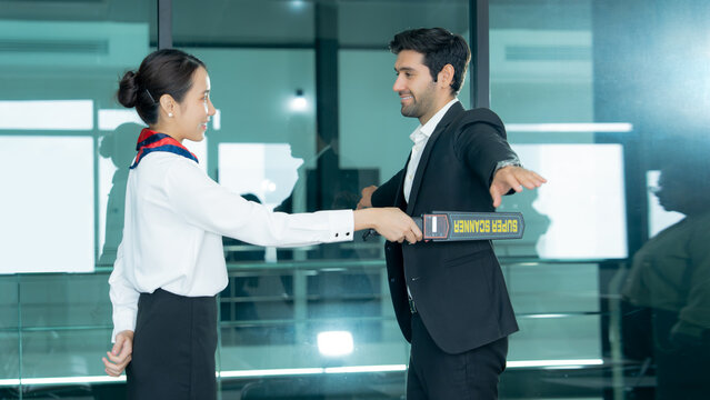  A security officer uses a handheld scanner to screen a businessman at an airport checkpoint highlighting passenger safety and access control. 