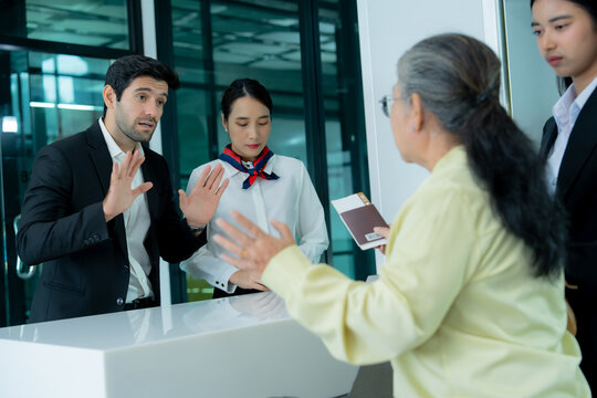 An older traveler expresses frustration while speaking with airport staff at a service counter representing customer complaints disagreement and conflict resolution.