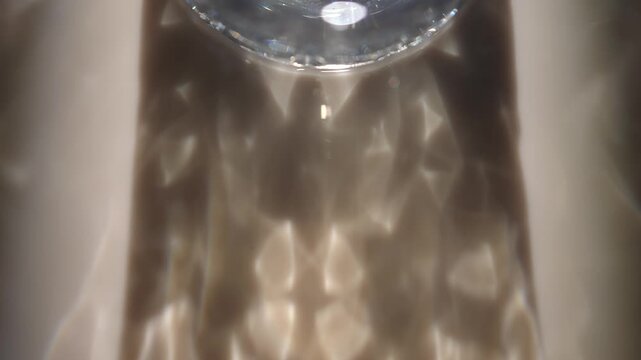 Glass rim casts soft golden reflections and caustic light patterns across a dark surface. Concept abstract optics for ads, websites, banners, magazines and presentations.
