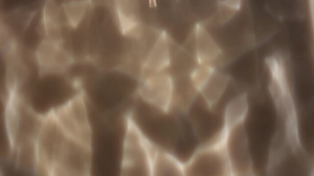 Soft warm caustic reflections create a blurred defocused abstract background with gentle light and shadow. Concept versatile backdrop for ads, websites, banners and presentations.