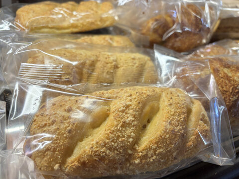 Close-up of freshly baked braided bread rolls with crumb topping individually wrapped in plastic packaging
