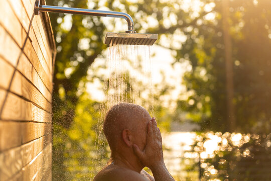 Man enjoying outdoor shower at sunset. Concept of evening relaxation and natural refreshment