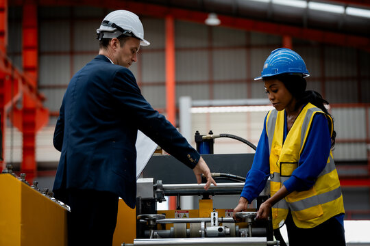 professional engineer, worker, technician use clipboard discuss work, walk in steel metal manufacture factory plant industry. Black African American man and woman wear hard hat check quality machine