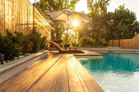 Swimming pool in modern private villa with lounge chairs, palm trees and umbrella