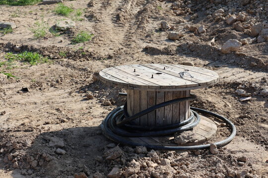 Wooden cable spool with black electrical wire lying on the ground of a construction site during utility infrastructure installation and municipal engineering works.