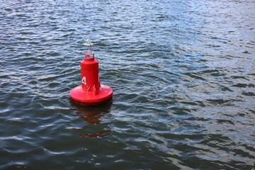 Red navigational buoy floating on rippling blue water of a river or sea, marine safety equipment © Алина Неборская