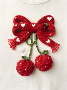 Red knitted heart bow with cherries and strawberries on white fabric background
