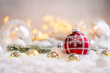 Naklejka premium A Christmas background featuring a red plaid bauble with a snowflake nestled among mirror disco balls and frosted pine on snow, softly lit by warm twinkling lights with copy space.