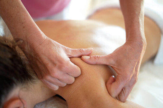 massage therapist massaging client's back in spa setting with pink shirt and white towel, relaxed and therapeutic mood, close-up from above the client's head, skin tone visible.