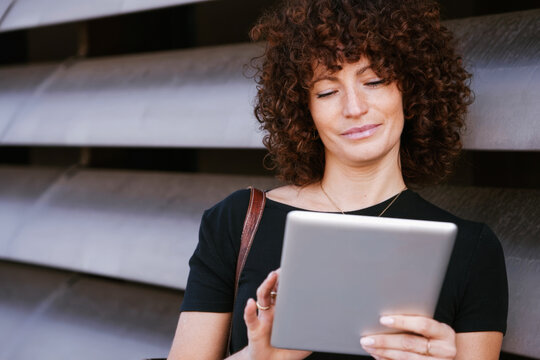 Female with curly hair casually enjoying digital entertainment in sunny city environment