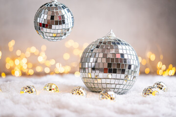 Naklejka premium A Christmas background featuring a large mirror disco ball surrounded by small reflective ornaments on snow, softly lit by warm twinkling lights, ideal for festive party designs with copy space.