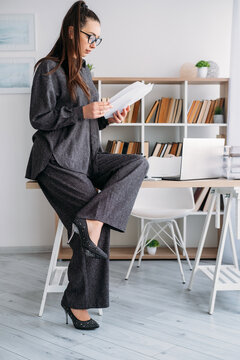 Office paperwork. Business lifestyle. Busy female expert reviewing document at desk with laptop at modern professional workspace.
