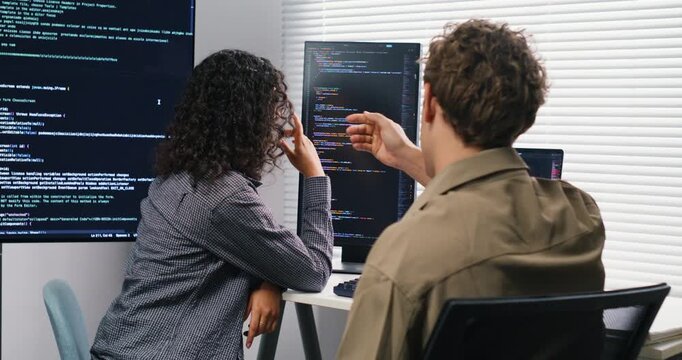  A male and female developer sit side-by-side, analyzing logs and stepping through code on dual monitors to reproduce and fix a runtime error.