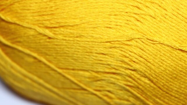 A small yellow ball of yarn on a clean white surface, ready for knitting or crafting. Rotating in a circle