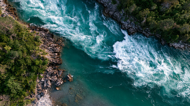 Aerial view of a turquoise river flowing through a rocky canyon with lush green forest. This powerful water flow represents energy and wild nature concepts.