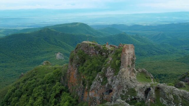 Aerial drone shot slowly flying away from the ancient kojori fortress ruins, also known as azeuli or korogli, perched on a dramatic mountain peak overlooking a vast, lush green valley in georgia