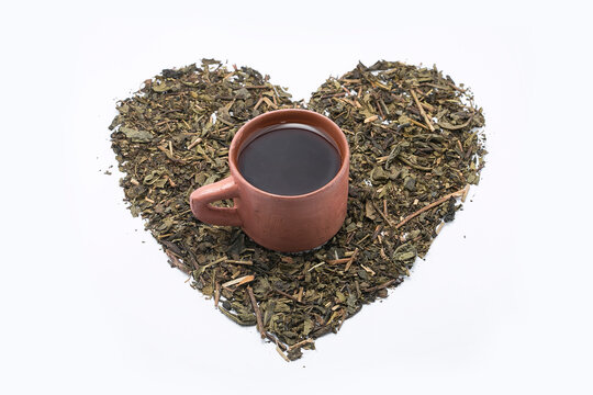 Close-up of a mug of fresh green tea on loose leaf green tea leaves arranged in a heart shape on a white background