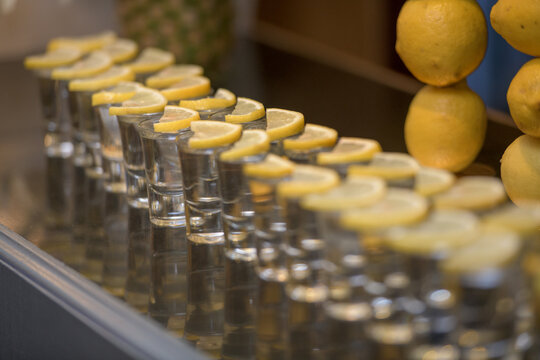 Close-up of a row of tequila shots with lemon slices in a bar area