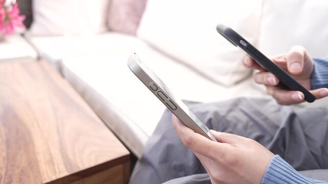 Middle-Aged Person Switching Between Two Smartphones At Home, Putting One Mobile Phone Down And Tapping The Other While Completing Data Transfer, Device Setup, Synchronization And Multitasking.
