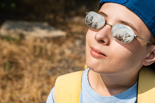 Close-up portrait of a teenage boy with a rural landscape reflected in his sunglasses on a summer day, Georgia