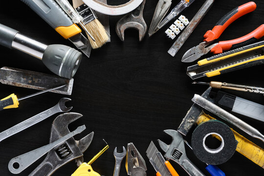 Assorted hand tools and repair supplies arranged around empty center on dark workshop surface