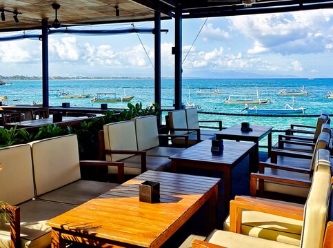 Open air beachfront cafe with an ocean view and traditional outrigger boats (jukung) anchored in the sea, Bali, Indonesia