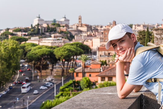 Smiling teenage boy leaning on a wall in Parco Savello with the city skyline in the background, Rome, Lazio, Italy