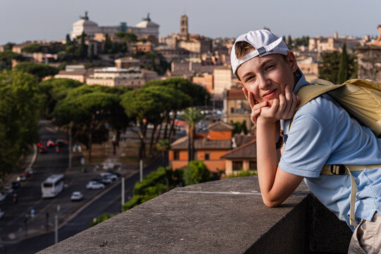 Smiling teenage boy leaning on a wall in Parco Savello with the city skyline in the background, Rome, Lazio, Italy