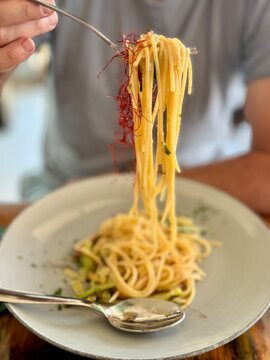 Close-up of a man sitting at a table eating a plate of saffron spaghetti with courgettes