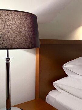 Close-up of an illuminated lamp on a bedside table by a double bed with luxury bedding