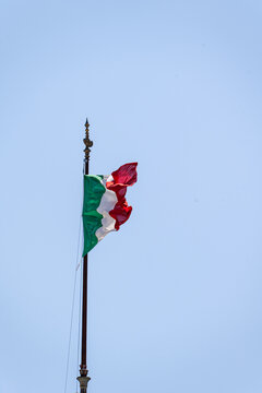 An Italian flag on a flagpole blowing in the wind with a blue sky background, Italy
