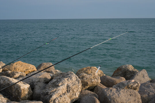 France, Valras Plage August 15, 2026 &mdash; Two fishing rods installed on rocky sea pier, ocean water horizon background, summer outdoor activity sport concept, desktop wallpaper search background