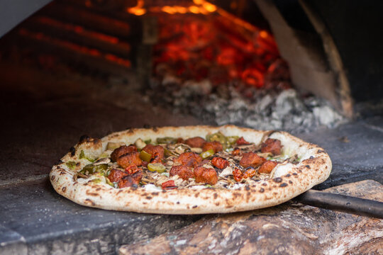 Pizza with meat baking in a wood-fired stone pizza oven with a roaring log fire in the back