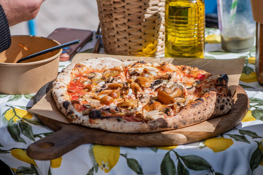 Freshly baked Neapolitan-style wood-fired pizza with forest mushrooms served on a wooden board over a lemon-patterned tablecloth