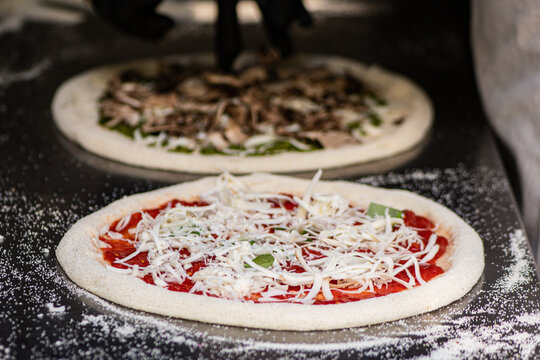 Pizza maker with black gloves preparing a Neapolitan-style pizza on a floured metal counter
