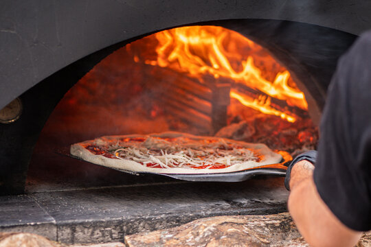 Pizza baking in a wood-fired stone pizza oven with a roaring log fire in the back