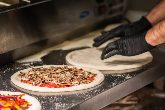 Pizza maker with black gloves preparing a Neapolitan-style pizza on a floured metal counter