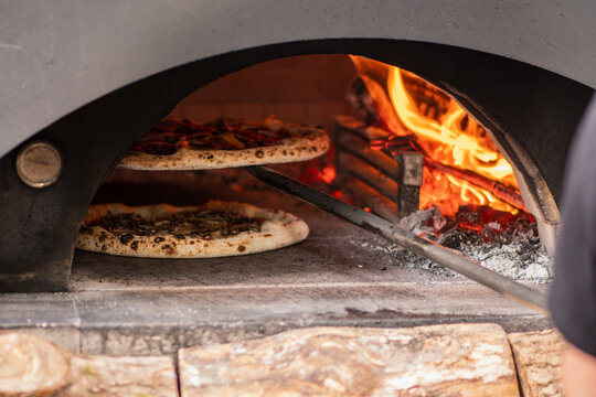 Pizzas baking in a wood-fired stone pizza oven with a roaring log fire in the back