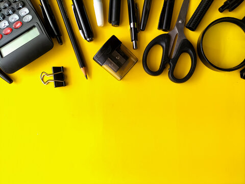 Black school and business stationery items scattered on a vivid yellow background