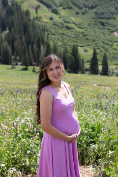 Portrait of a smiling pregnant woman in a summer dress standing in an alpine landscape, Albion Basin, Little Cottonwood Canyon, Utah, USA