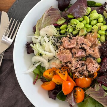 Close-up overhead view of a salad with tuna, edamame beans, beetroot, cherry tomatoes, spring onion and black sesame seeds on a table with cutlery