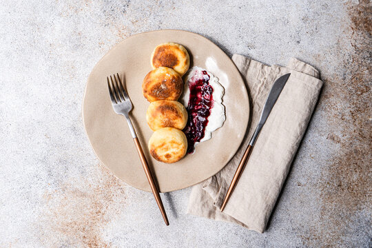 Close-up overhead view of  a plate of sweet Syrniki pancakes with sour cream and blueberry jam on a concrete table