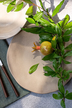 Close-up overhead view of an Autumnal place setting decorated with a fresh pomegranate branch and fruit
