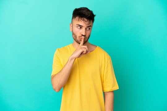 Young caucasian man isolated on blue background showing a sign of silence gesture putting finger in mouth